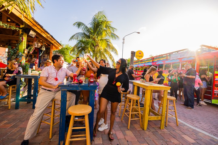 People enjoying drinks at colorful outdoor venue with a bright bus in the background.