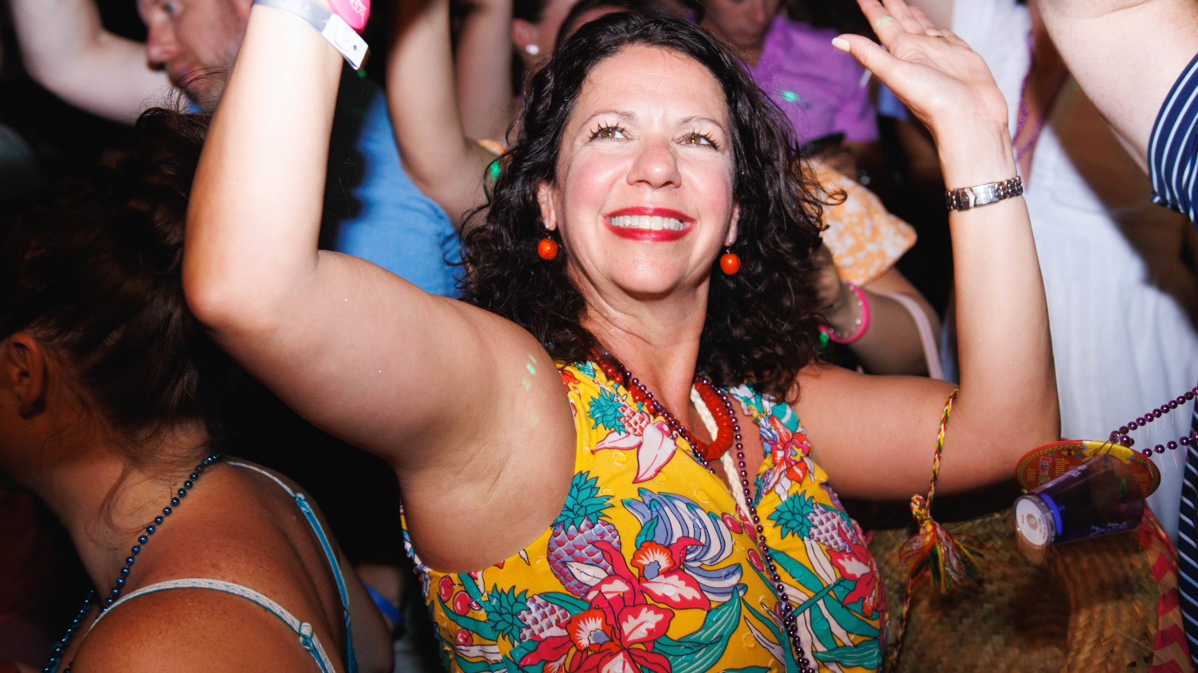 Woman in floral dress dancing joyfully at a party with raised arms, surrounded by other people.