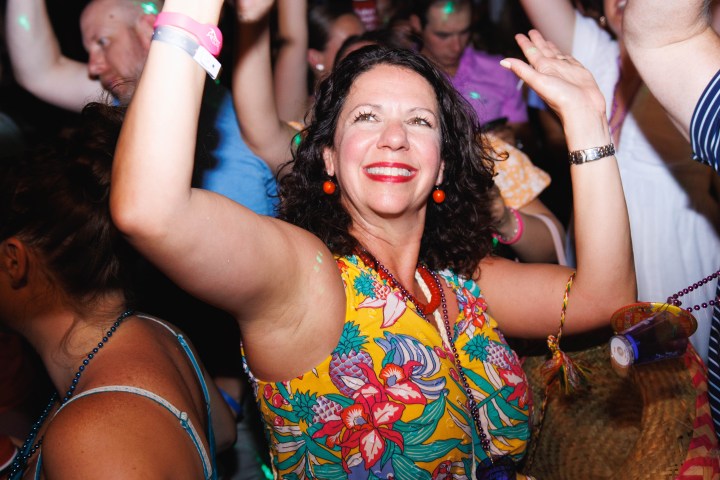 Woman in floral dress dancing joyfully at a party with raised arms, surrounded by other people.