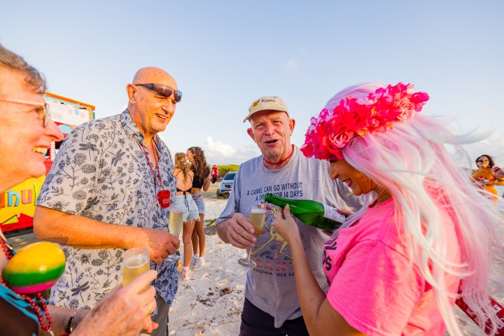 Group of people smiling and holding drinks at a beach party.