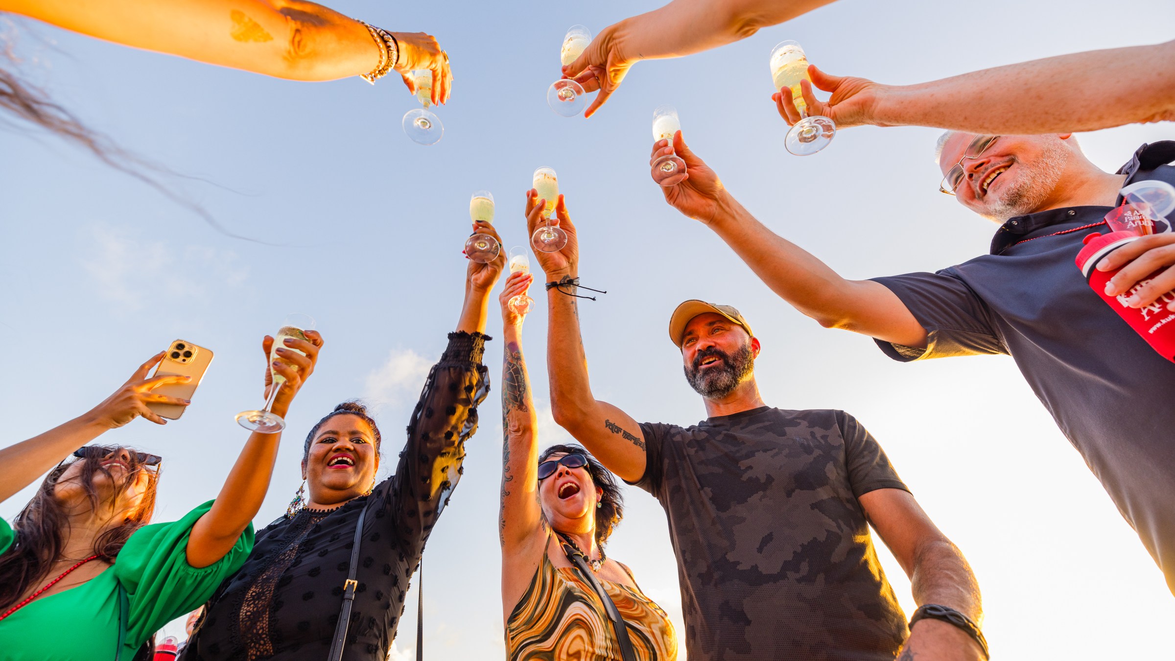 People raising glasses in celebration outdoors under a clear sky.