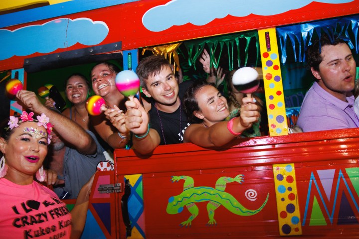Group of people on a colorful party bus, holding maracas and smiling, festive atmosphere.