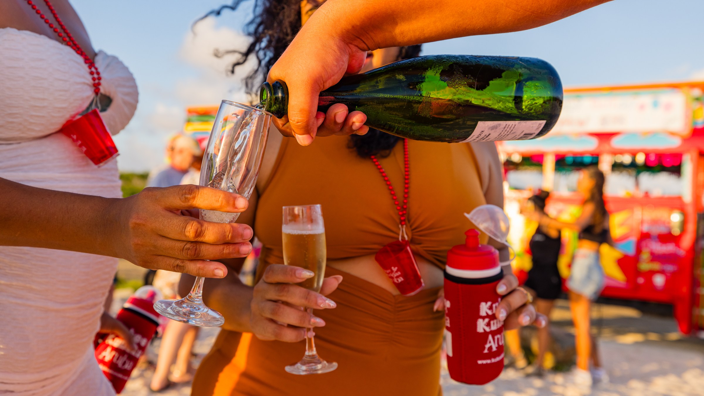 People pouring champagne into glasses on a beach with a party bus in the background.