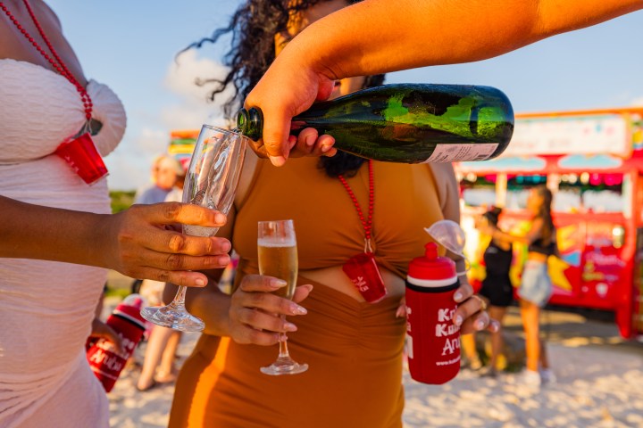 People pouring champagne into glasses on a beach with a party bus in the background.