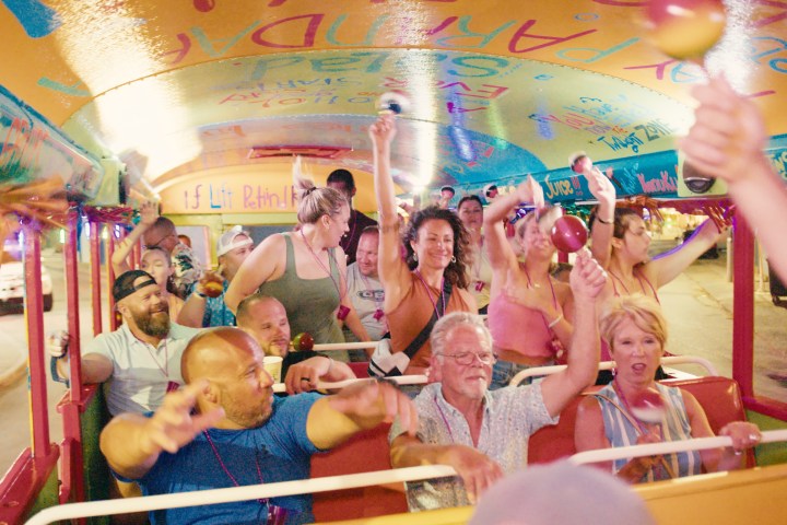 Group of people having fun inside a colorful party bus, holding maracas and dancing.