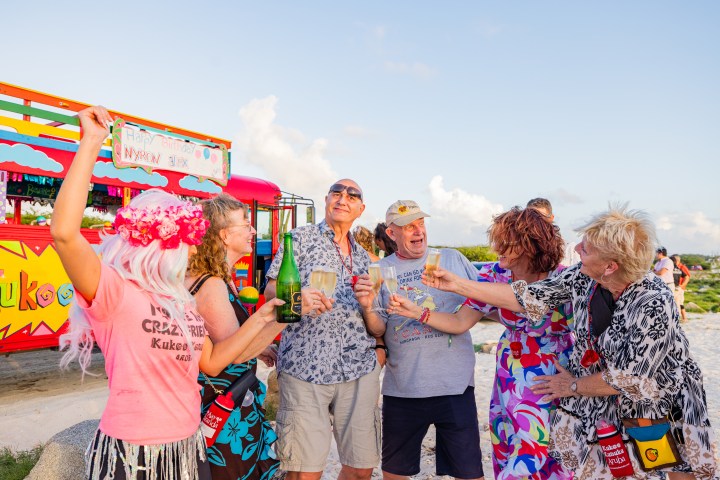 Group of people celebrating with drinks in front of a colorful bus on a bright day.