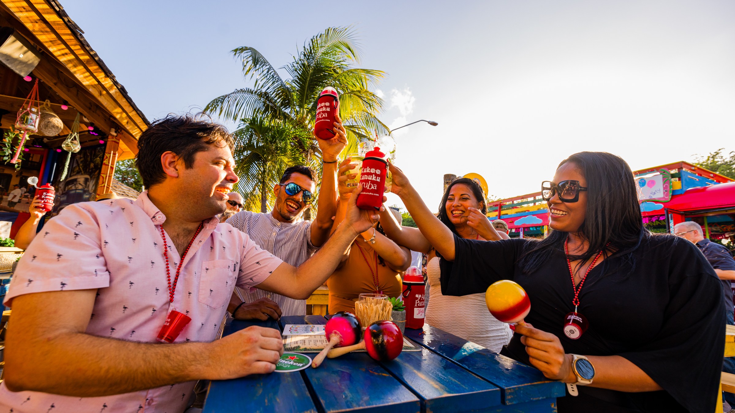 Group of people toasting with drinks at an outdoor festival under palm trees.