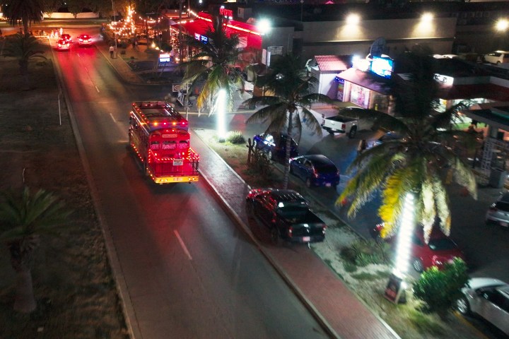 Night street view with bright red buses, palm trees, and illuminated shops.