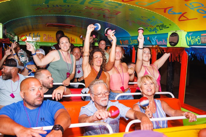 Group of people on a colorful party bus, holding maracas and smiling.