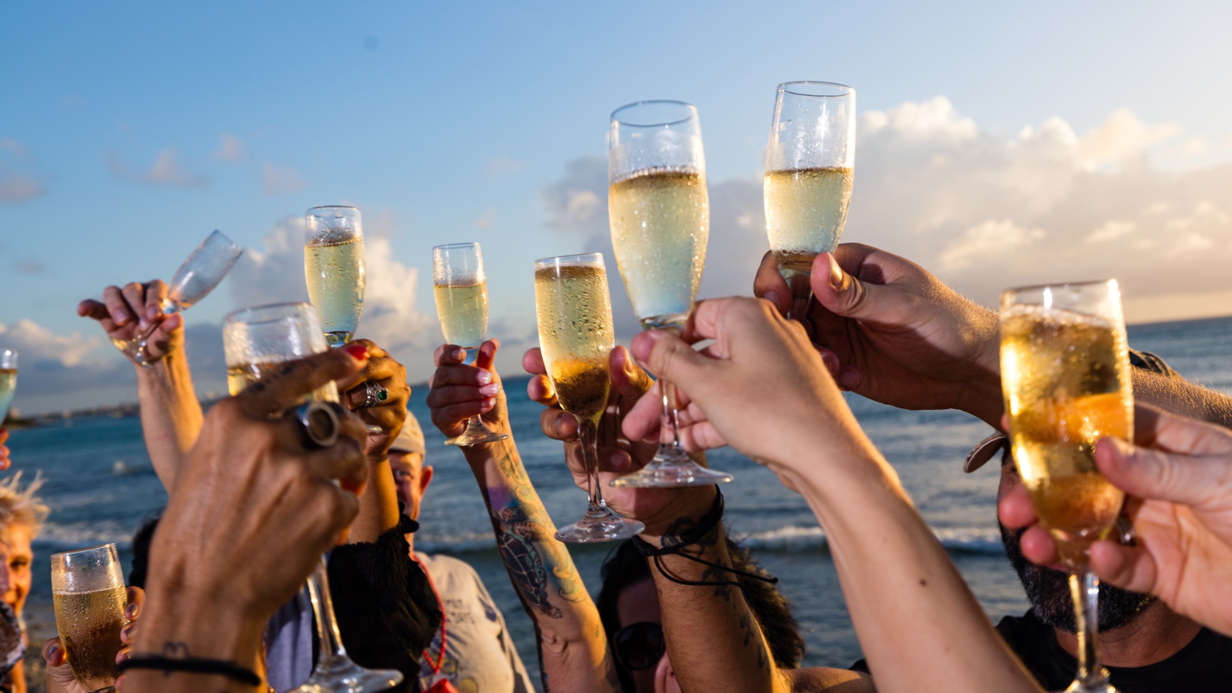 Group of people toasting with champagne glasses by the seaside at sunset.