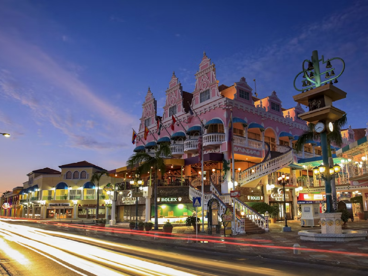 Colorful shopping complex with lights at dusk, long exposure car trails on street.