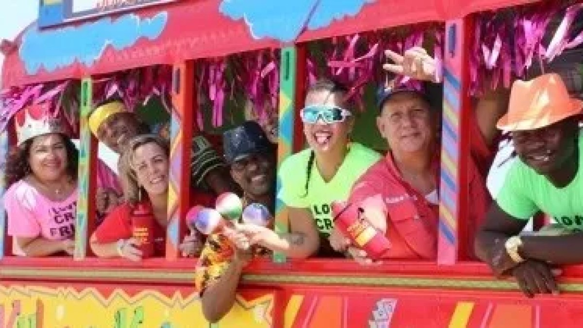 Group of people in colorful attire smiling on a vibrant carnival bus.