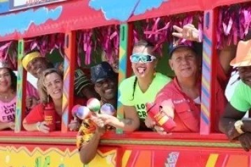 Group of people in colorful attire smiling on a vibrant carnival bus.