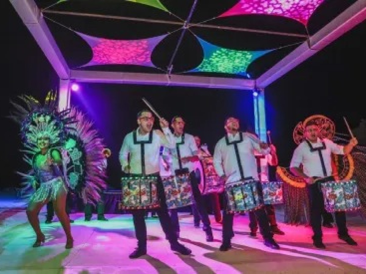 Colorful dancers and drummers perform under vibrant lights and a decorated canopy at night.