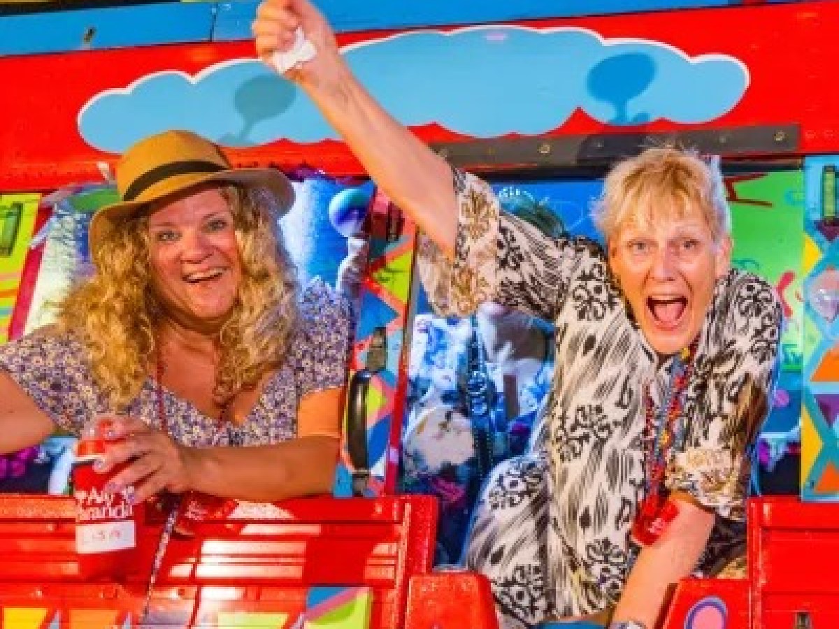 Two women enjoying a colorful, vibrant ride, one with a maraca and hat, the other with a joyful expression.