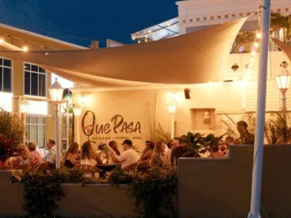 Outdoor restaurant with people dining under string lights at night.