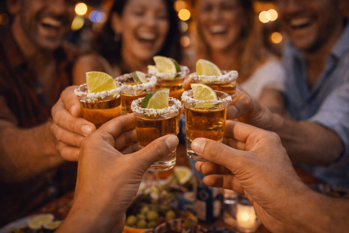 Group toasting with salt-rimmed tequila shots and lime, smiling and celebrating together.