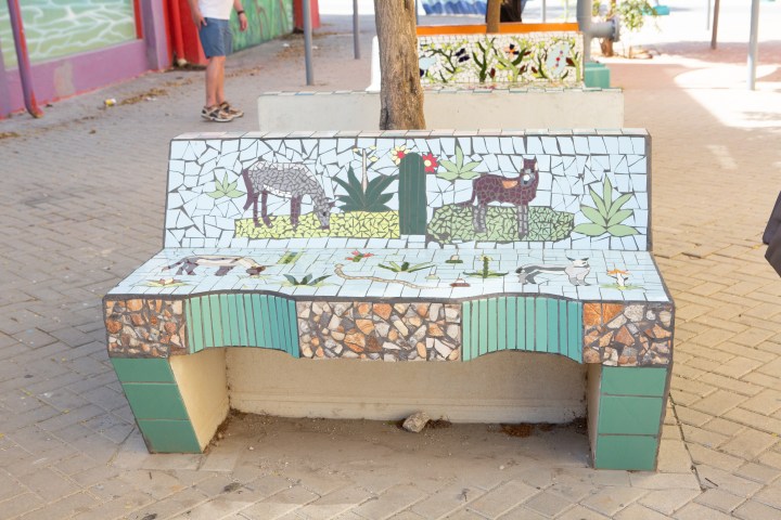 Mosaic bench with animal and plant designs in a park.
