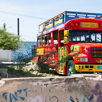 Colorful bus parked outdoors with bright patterns and nearby greenery.