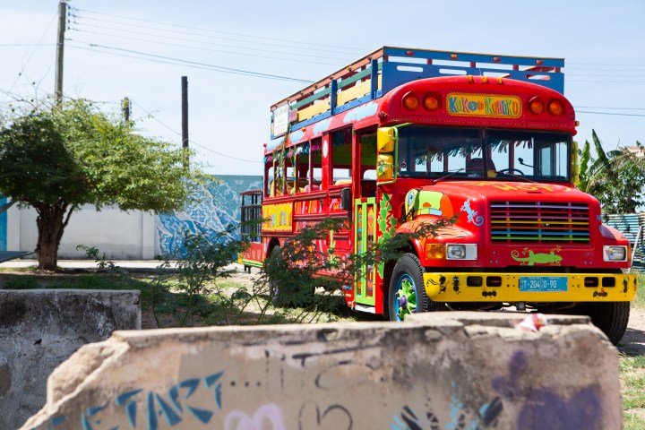 Colorful bus parked outdoors with bright patterns and nearby greenery.