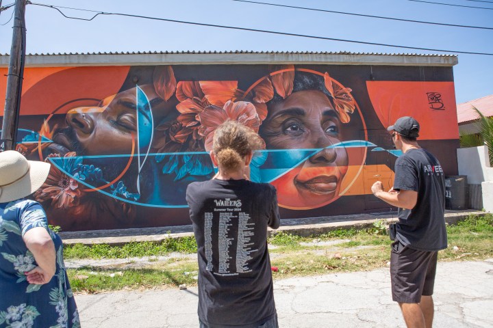 People admire a vibrant mural featuring faces with floral elements.