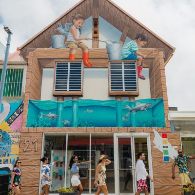 Building with murals of children and fish, people walking by on the street.