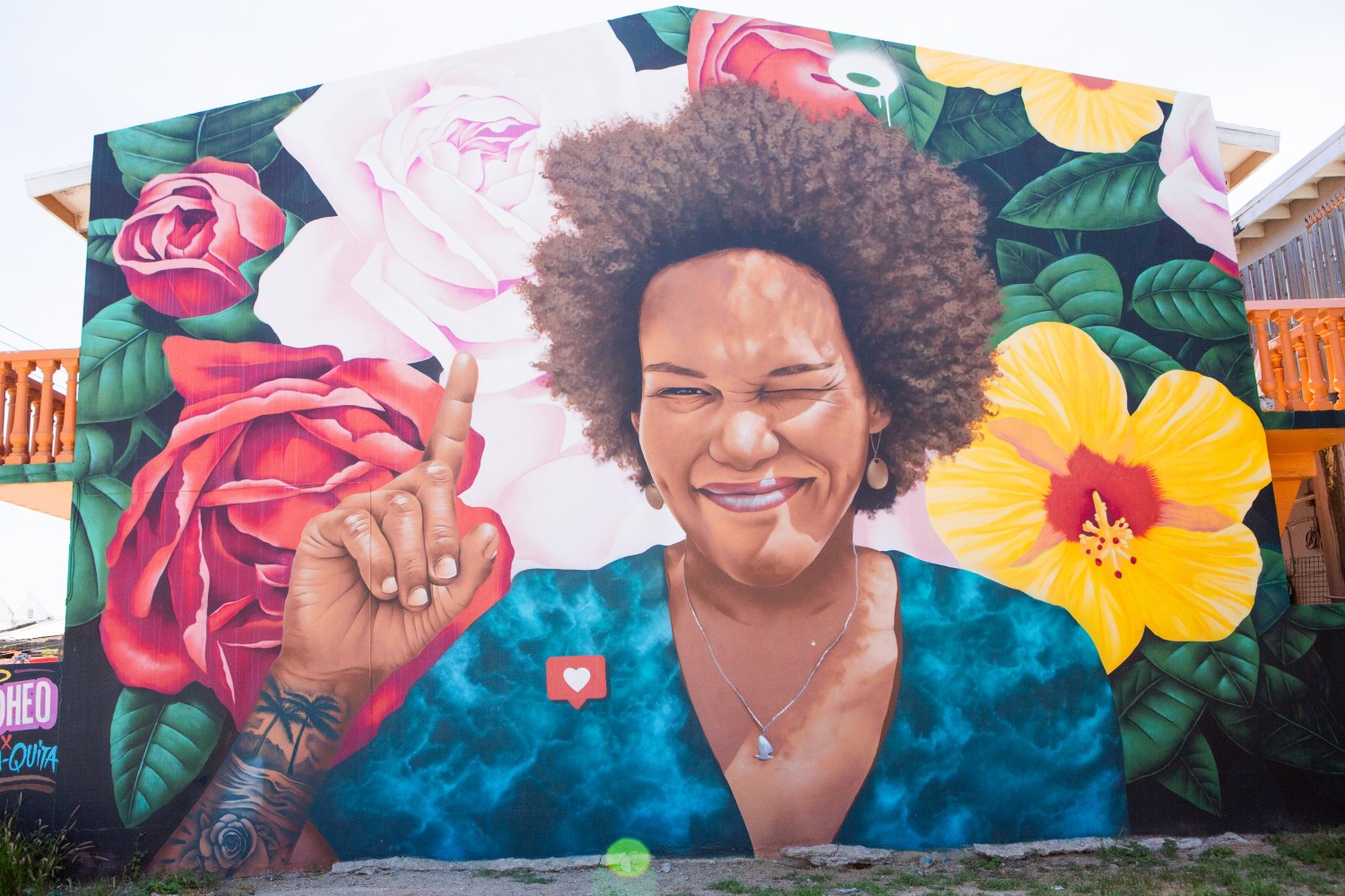 Colorful mural of a smiling person with flowers, raising an index finger.