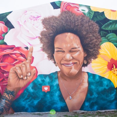 Colorful mural of a smiling person with flowers, raising an index finger.