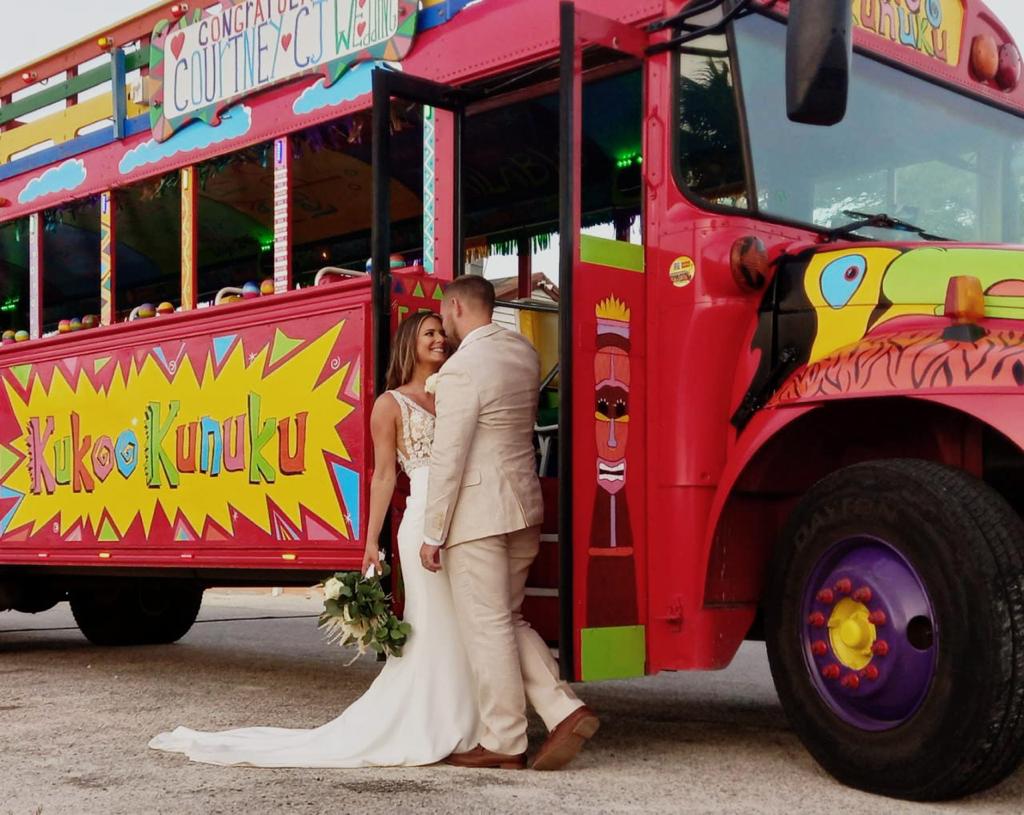 Bride and groom kissing in front of a colorful party bus.
