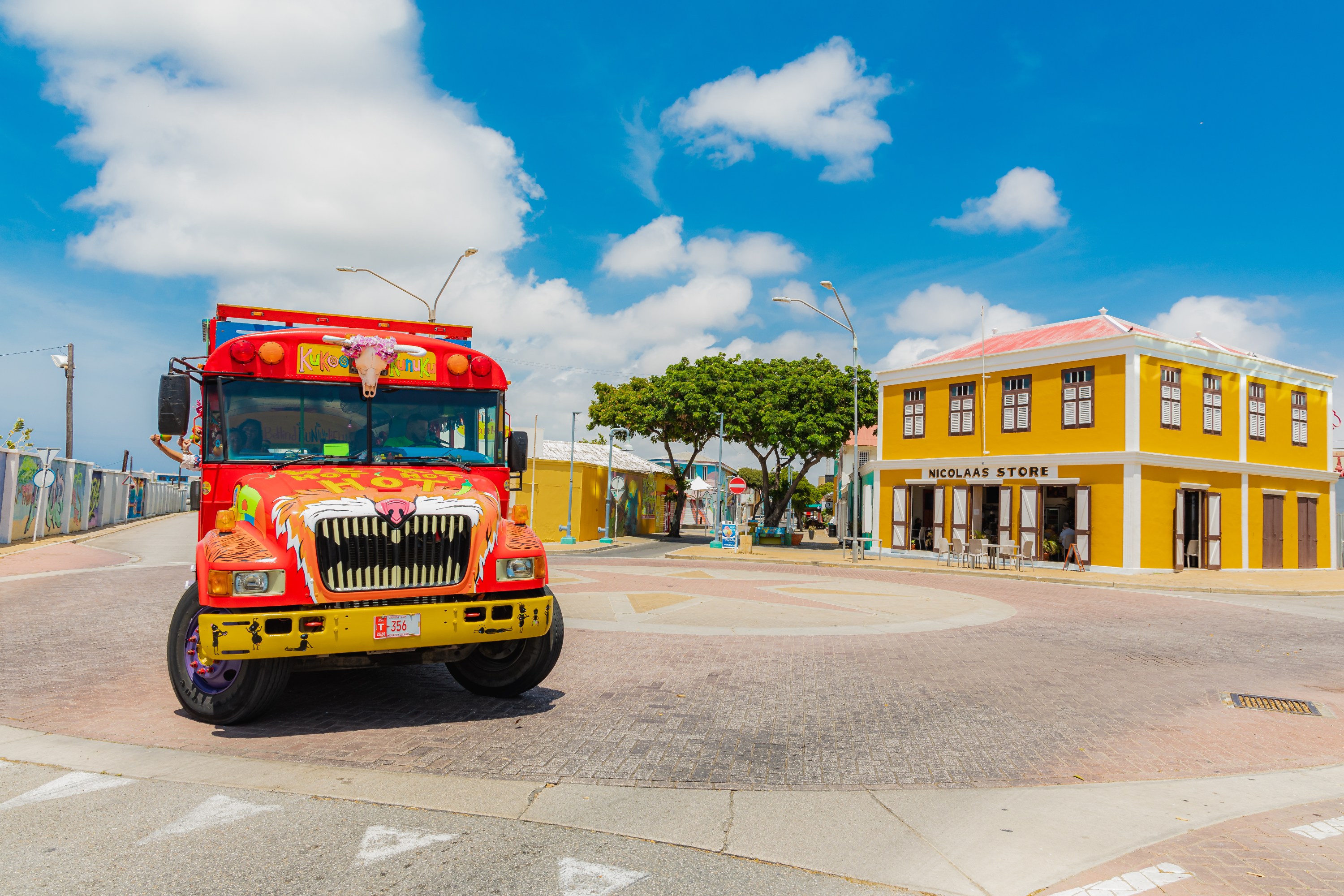 Colorful bus and yellow building under a bright blue sky with clouds.