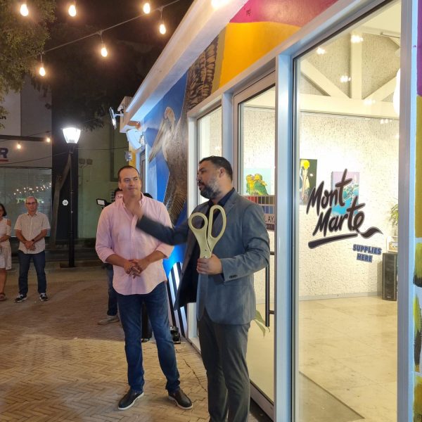 Two people stand outside a shop, one holds oversized scissors.