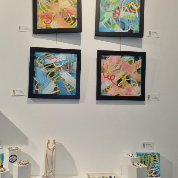 Four abstract paintings and jewelry displayed in a gallery setting.