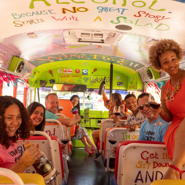 Happy group of people inside a colorful bus, holding drinks and smiling.