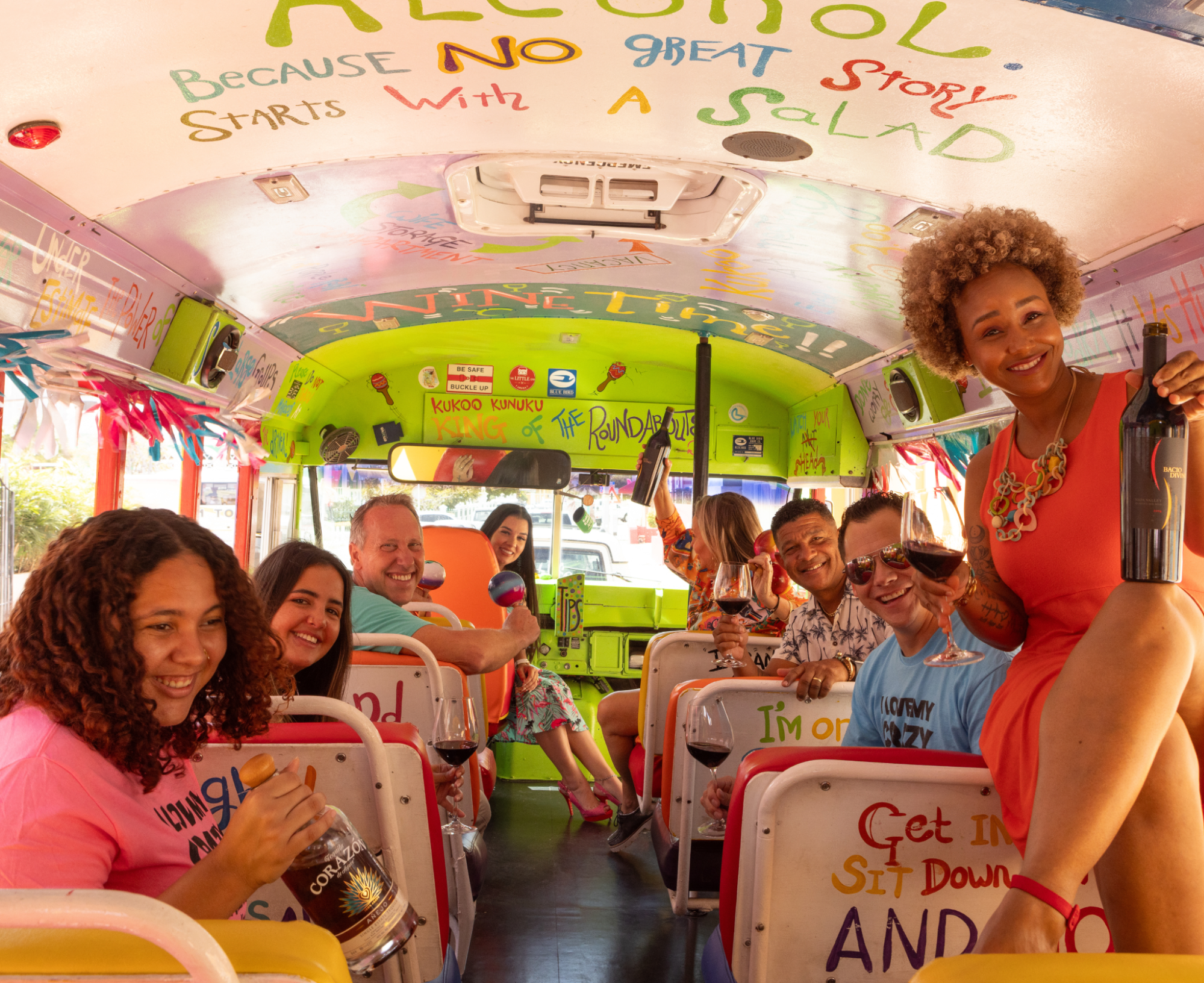 People smiling and holding drinks in a colorful, decorated bus.