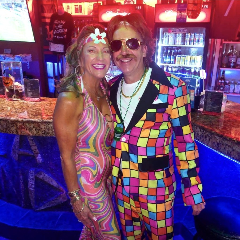 Couple dressed in colorful retro costumes enjoying a Kukoo Kunuku Halloween celebration in Aruba.