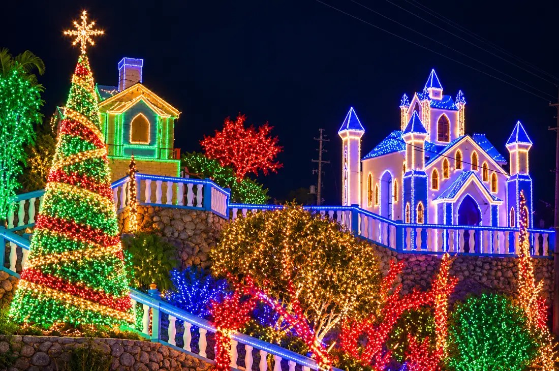 Cas di Luz illuminated blue castle, Christmas tree, and hillside decorations at night.